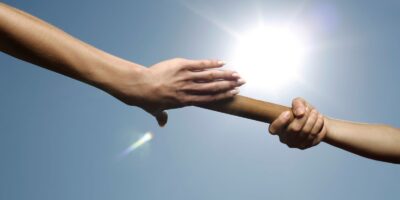 Two hands passing a baton under a bright sun, symbolizing teamwork and cooperation.